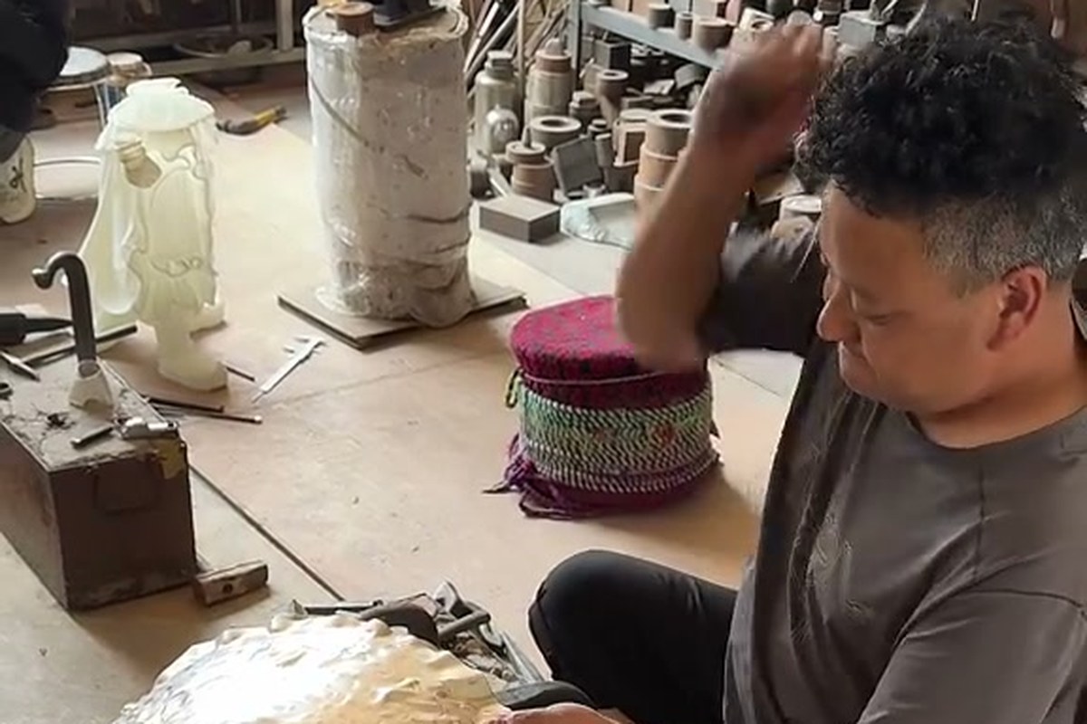 Silversmith hammering a large silver vessel at a workbench
