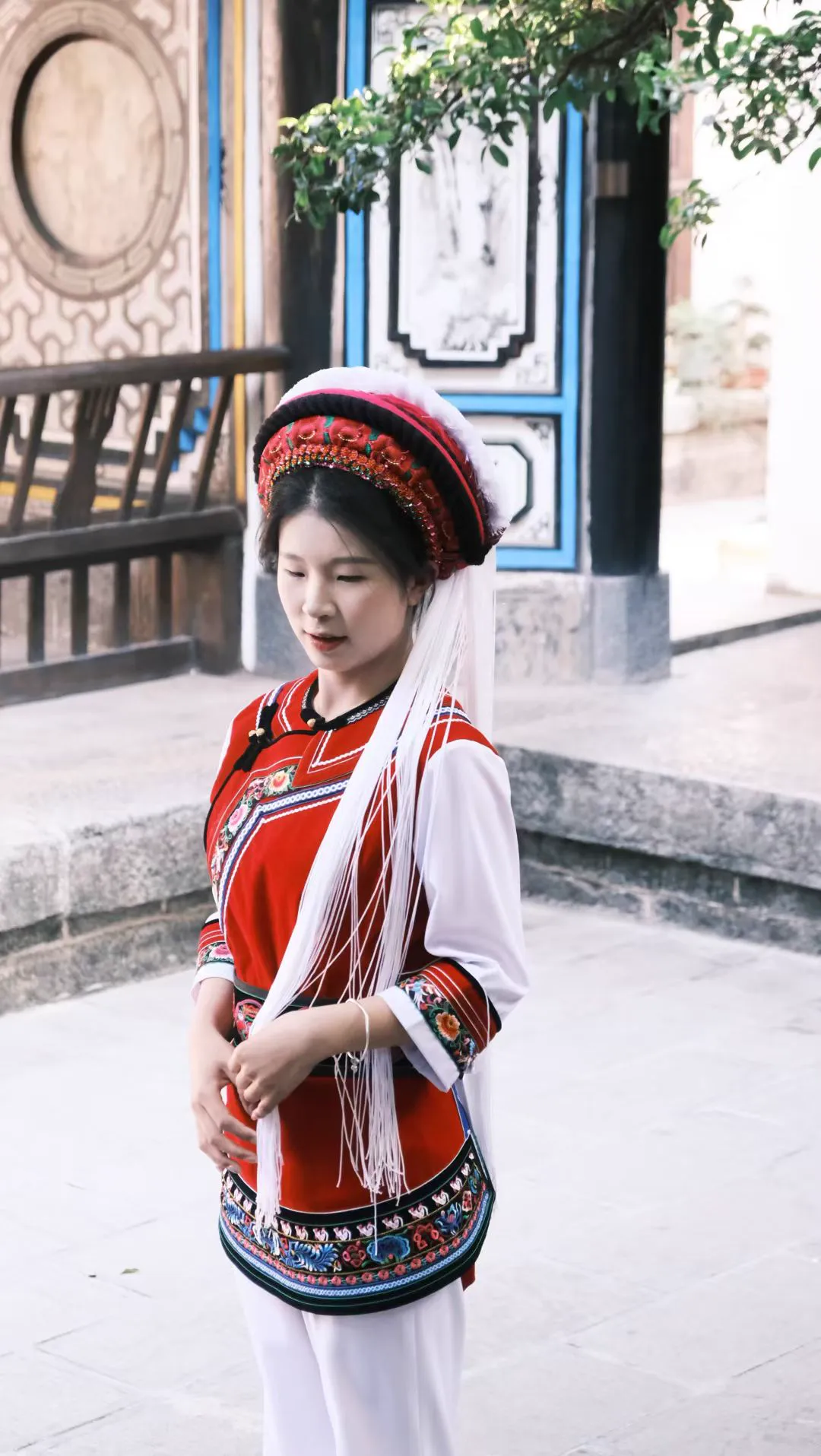 Bai girl in red before traditional building